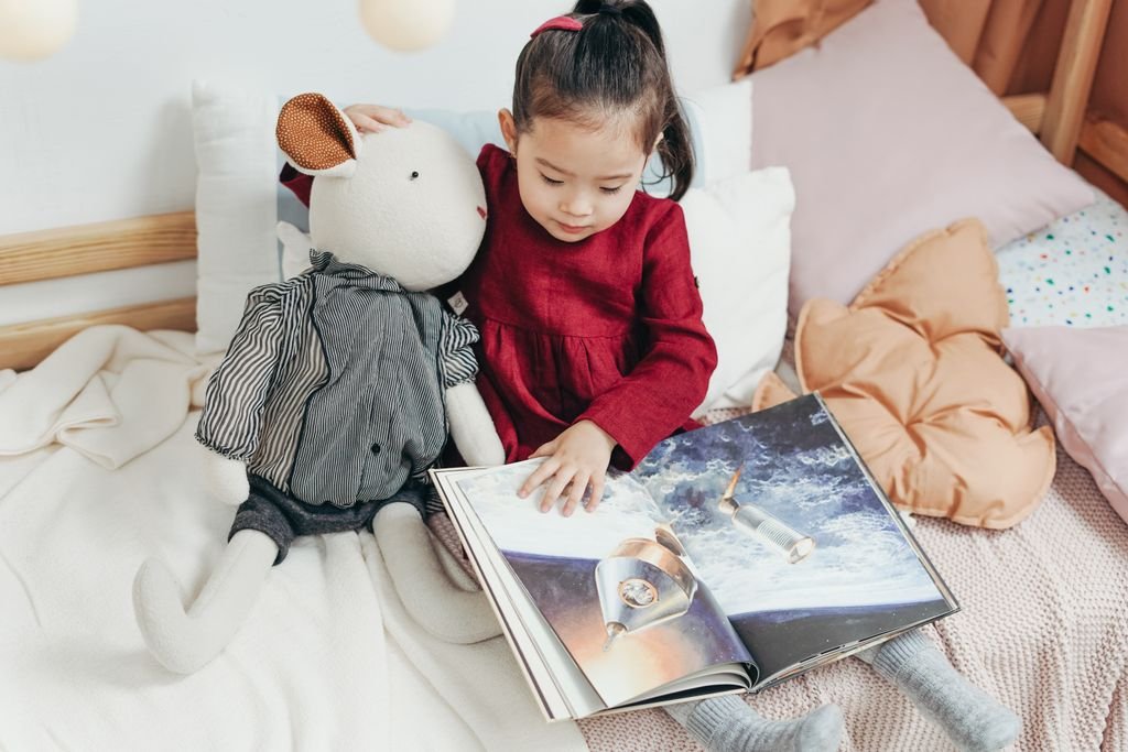 Child reading a picture book with a stuffed toy in a cozy bedroom setting.